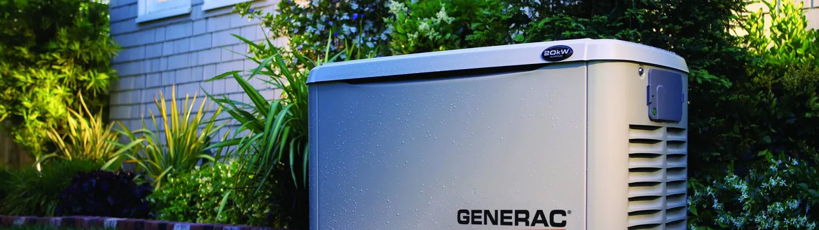 Generac Guardian Series home standby generator installed on a brick platform in a landscaped yard beside a house.