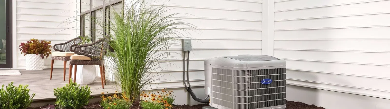 Residential outdoor air conditioning unit next to a white house with landscaped garden and green lawn.