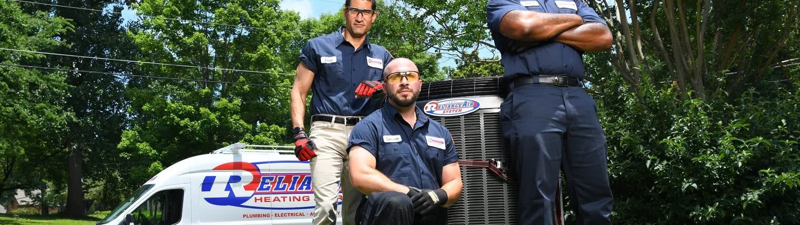 Three HVAC technicians posing outdoors by an air conditioner unit with a company van in the background.