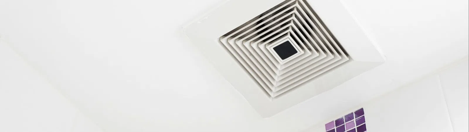 Ceiling ventilation fan with a geometric grille against a white background and purple tiled wall.