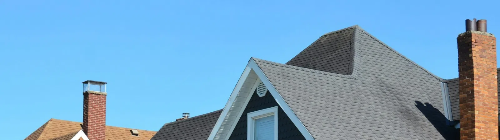 Gray house with white trim, stone porch pillars, chimney, and well-kept front yard under clear blue sky