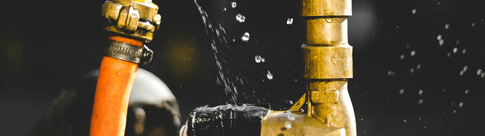 Close-up of an old brass water faucet with orange hose leaking water drops against dark background