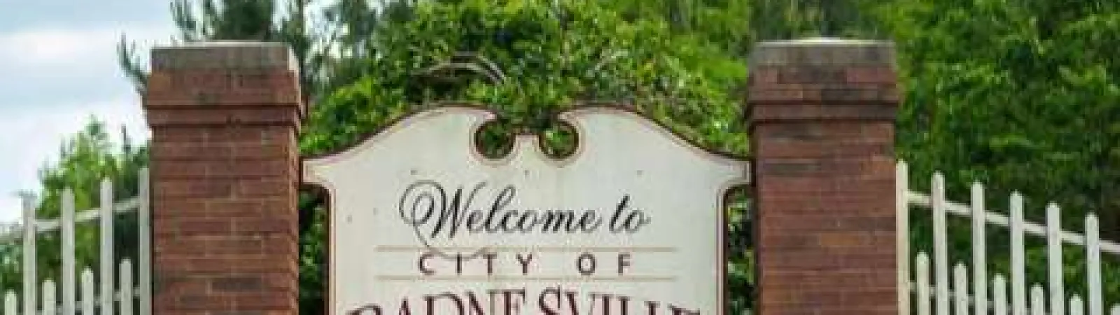Welcome sign for the City of Barnesville with brick pillars and green shrubs under a partly cloudy sky