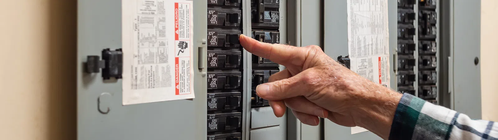 Close-up of a hand pointing at electrical circuit breakers in a residential panel.