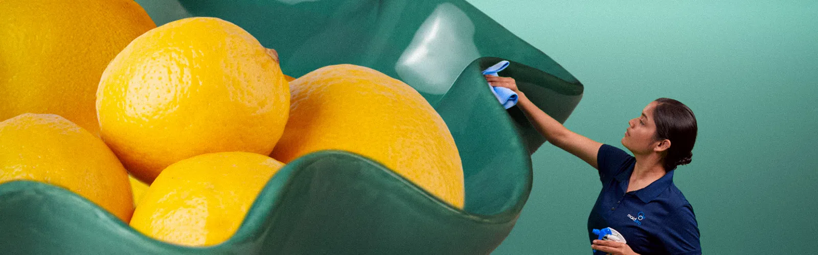 A woman cleans a giant green bowl filled with oversized lemons, kneeling beside large lemon halves on mint background.