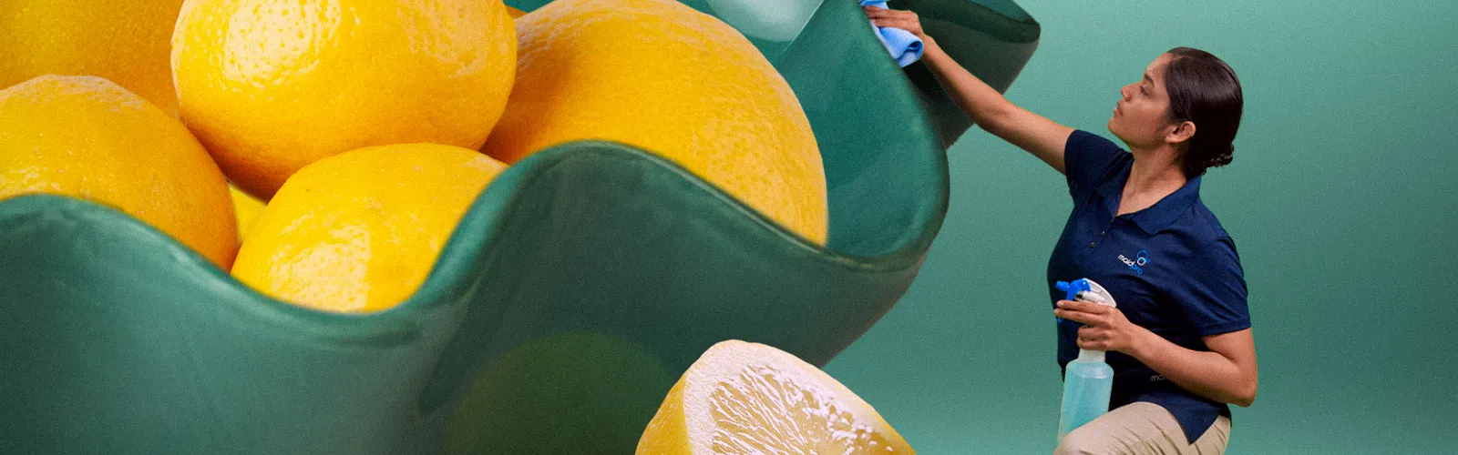 Woman cleaning an oversized green bowl filled with giant lemons and a lemon half on a teal surface and background