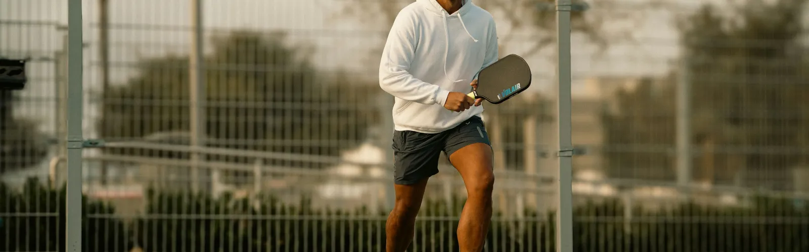 Man in white hoodie playing pickleball on outdoor court 2 during daytime