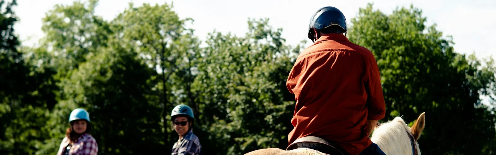 Two people wearing helmets smiling and riding bicycles on a sunny suburban street with greenery and houses.