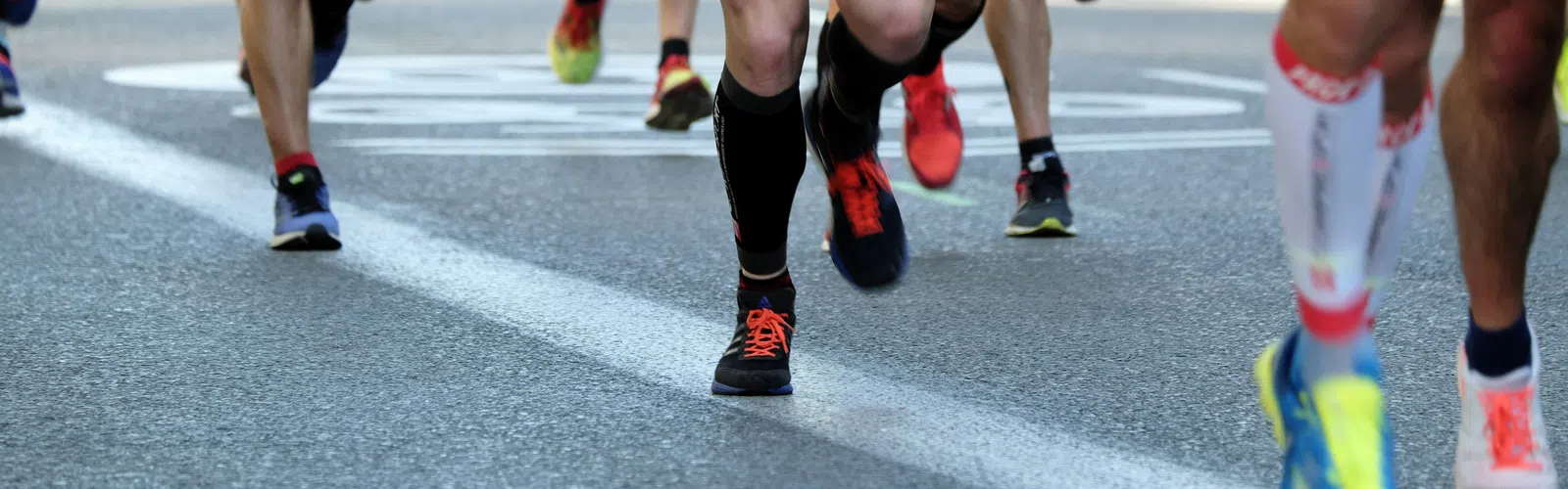 Close-up of runners' legs and feet during a race, showing diverse running shoes on an asphalt road