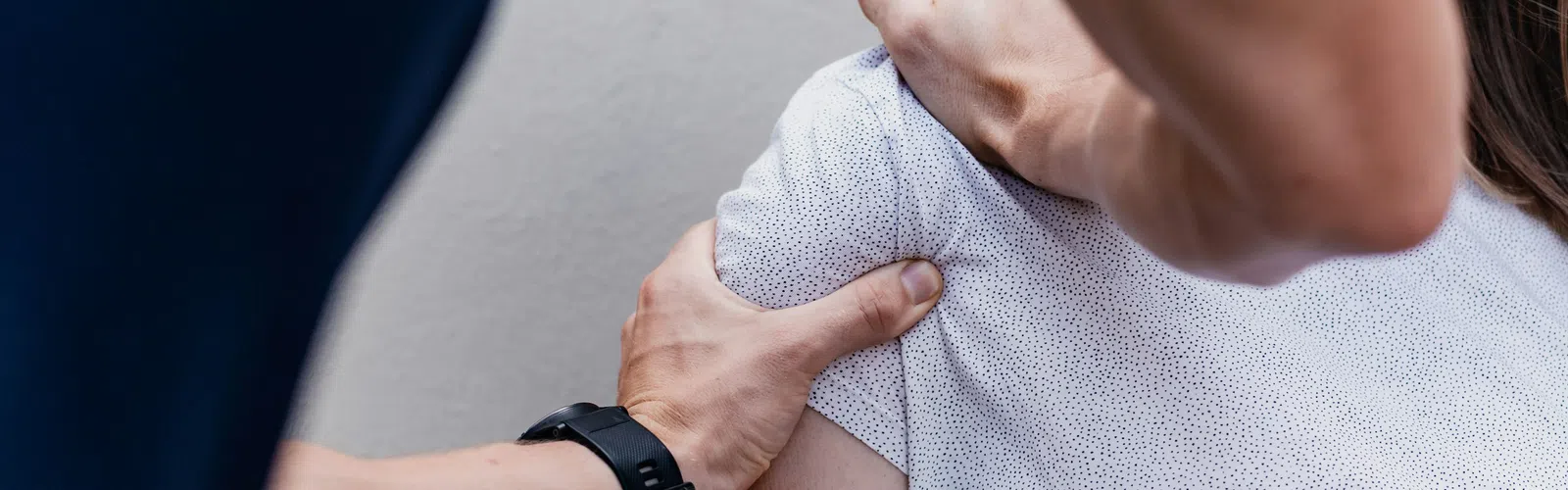 Physical therapist assessing woman's shoulder mobility with hands on her arm and upper back.