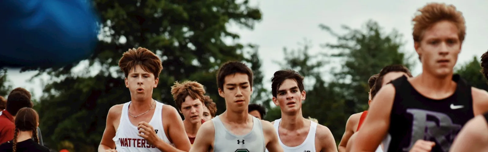 High school cross country runners competing in a race on a grassy field.