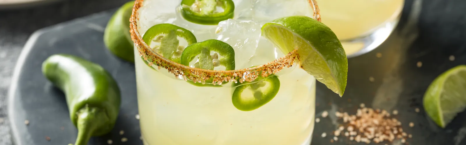 a glass of liquid with limes and a slice of lime on a black surface