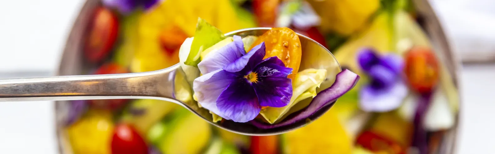 Edible flower violas on spoon over a salad