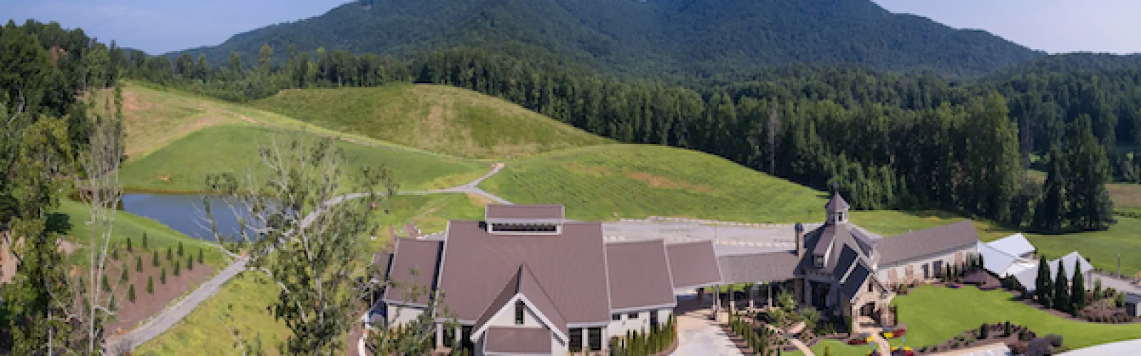 Aerial view of a countryside building complex with mountains and greenery under a clear blue sky.