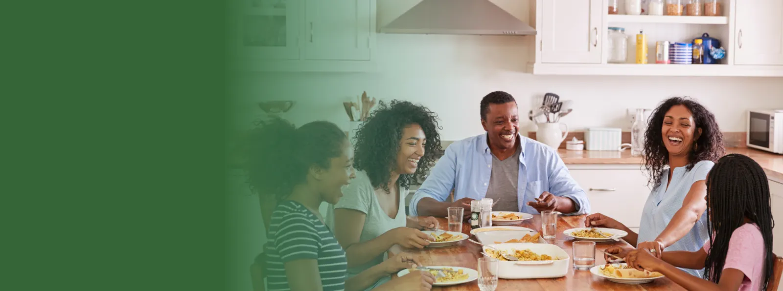 Family of five enjoying a meal together and laughing around a wooden table in a bright kitchen