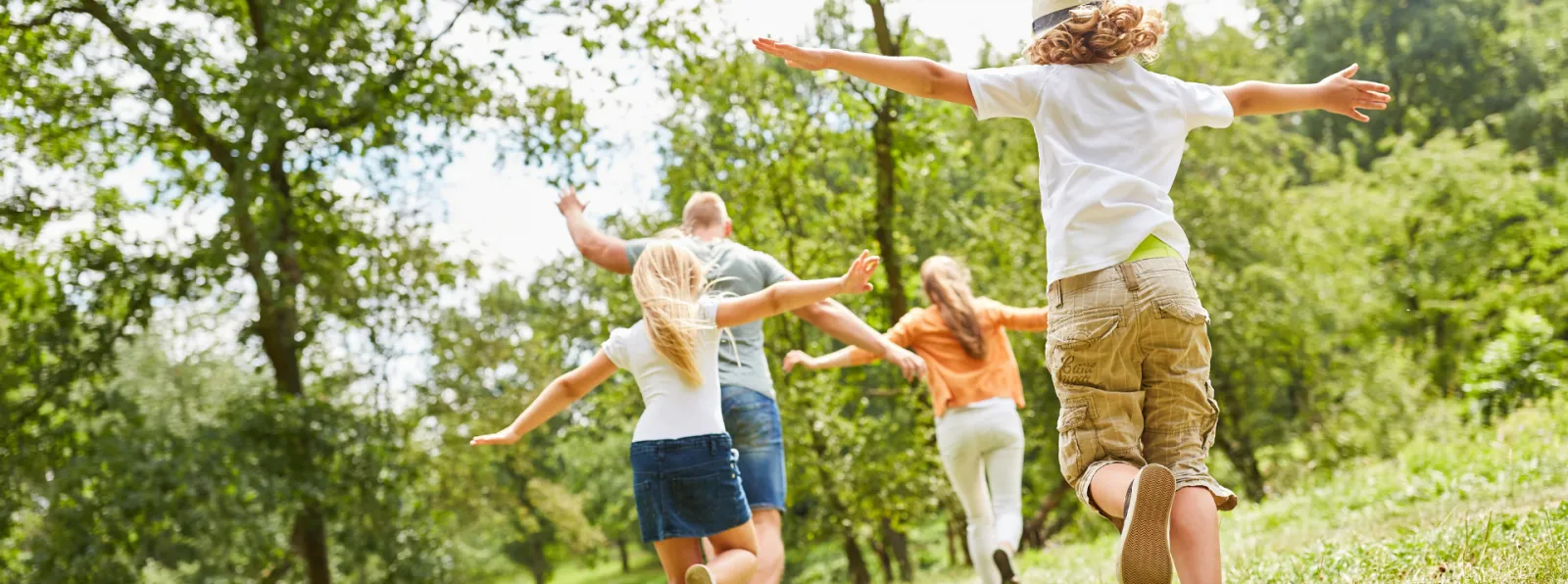 Children running with arms outstretched in a green park on a sunny day, enjoying outdoor play and nature.
