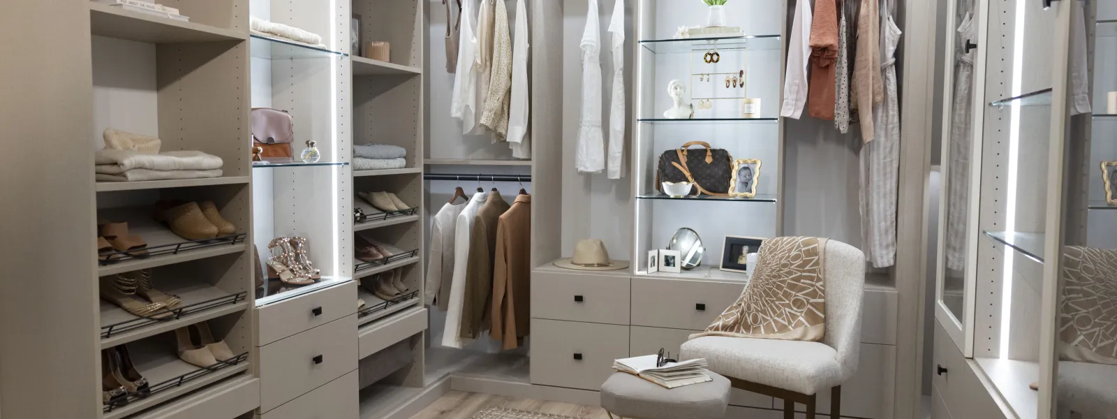 a custom designed womans closet with neutral tones and black hardware