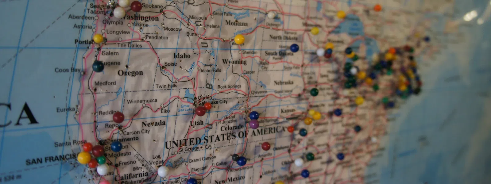 Colorful push pins marking locations on a world map with a blurred background and focused pins.