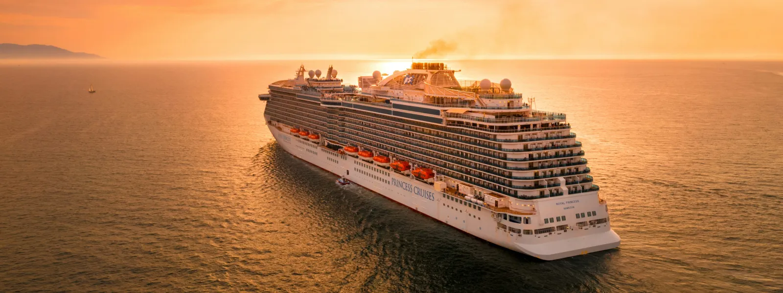 Luxury cruise ship sailing on calm ocean waters during a vibrant orange sunset with clear skies.