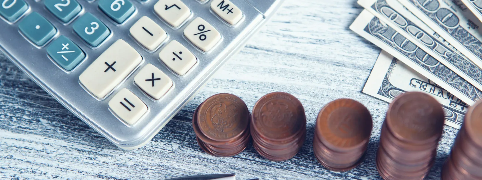 Calculator, stacked coins, and US dollar bills on a wooden surface with a pen, representing financial management.