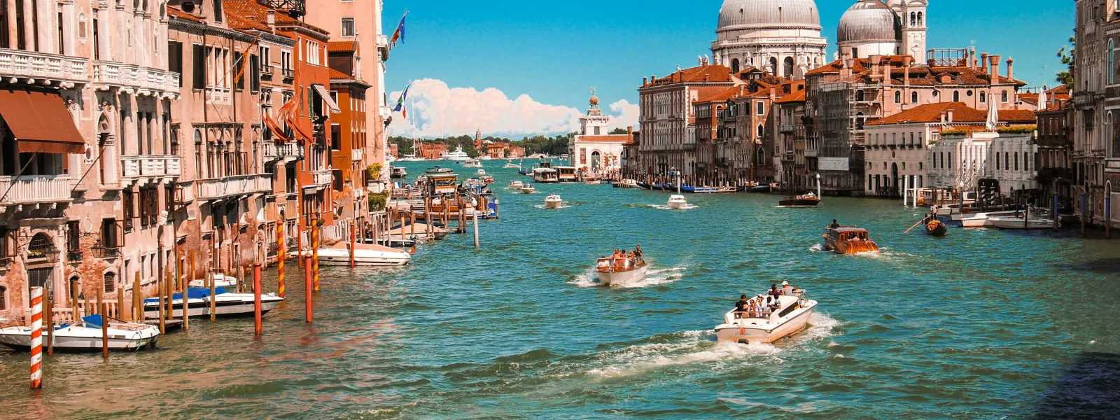 Grand Canal in Venice with historic buildings, boats cruising the waterway and blue sky with clouds.