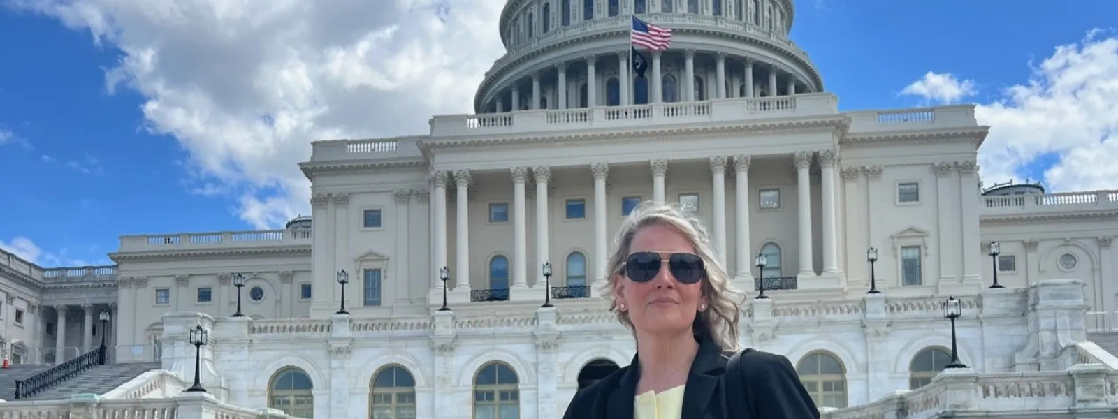 Professional woman in sunglasses standing in front of the United States Capitol building on a sunny day