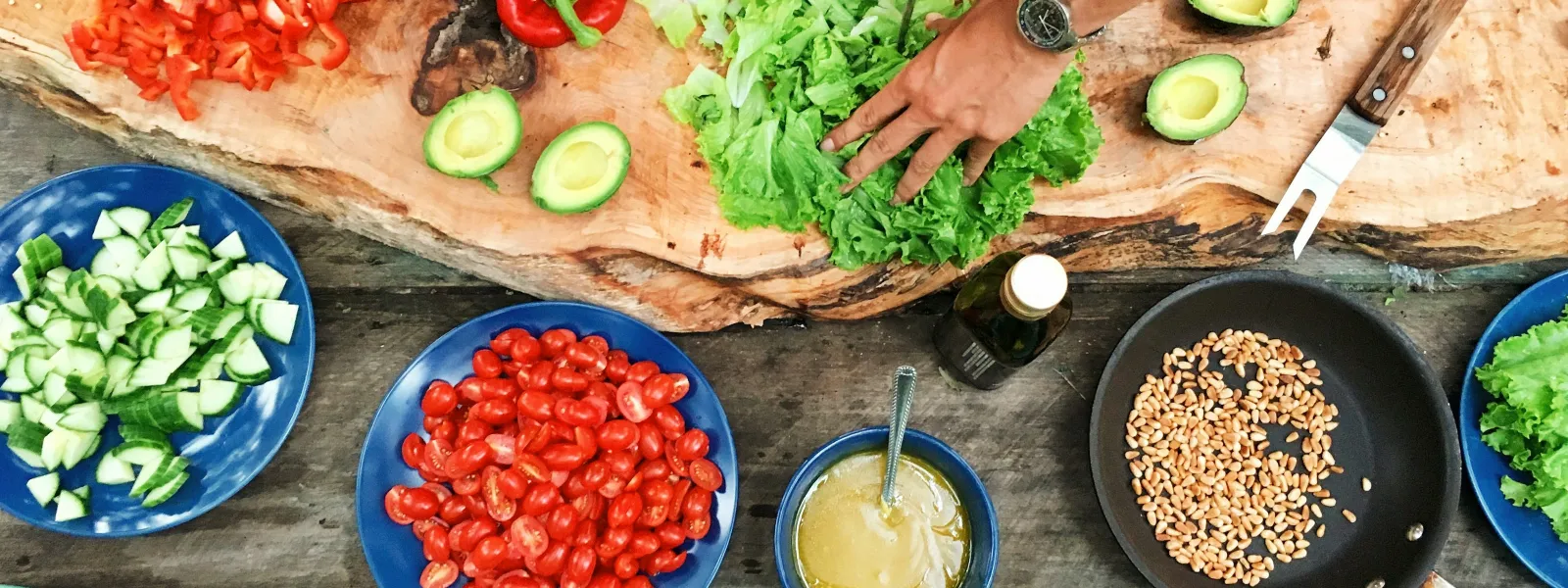 Fresh vegetables being chopped and prepared on a wooden table with various bowls and a blue paddle.