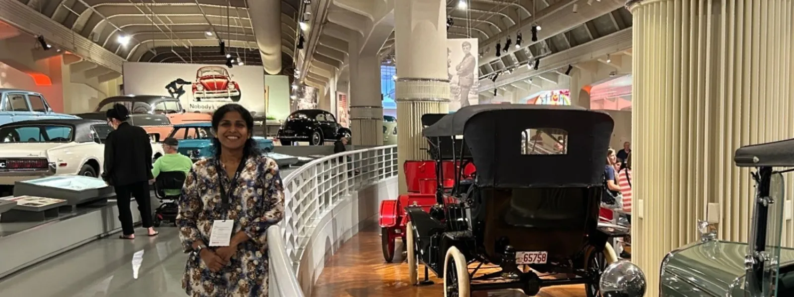 Historic vintage cars displayed in museum with wooden floors and visitors viewing exhibits.