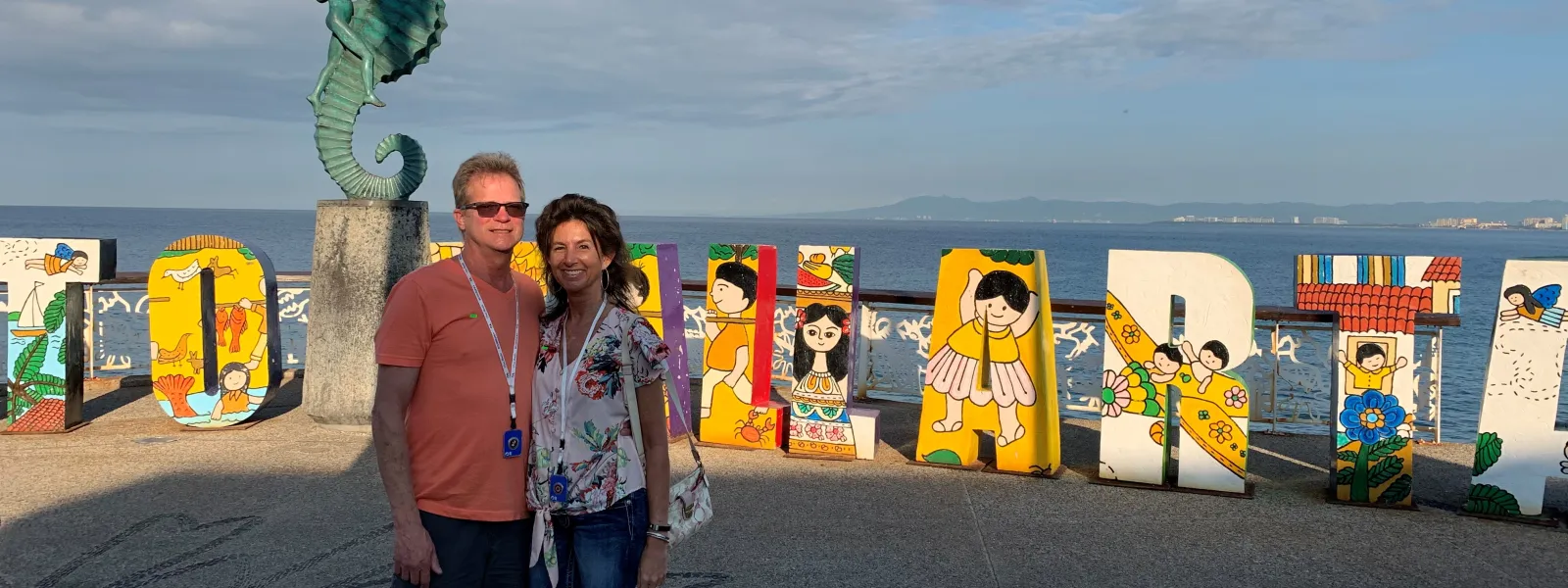 Couple posing in front of colorful Puerto Vallarta letters and seahorse statue by the ocean on a sunny day