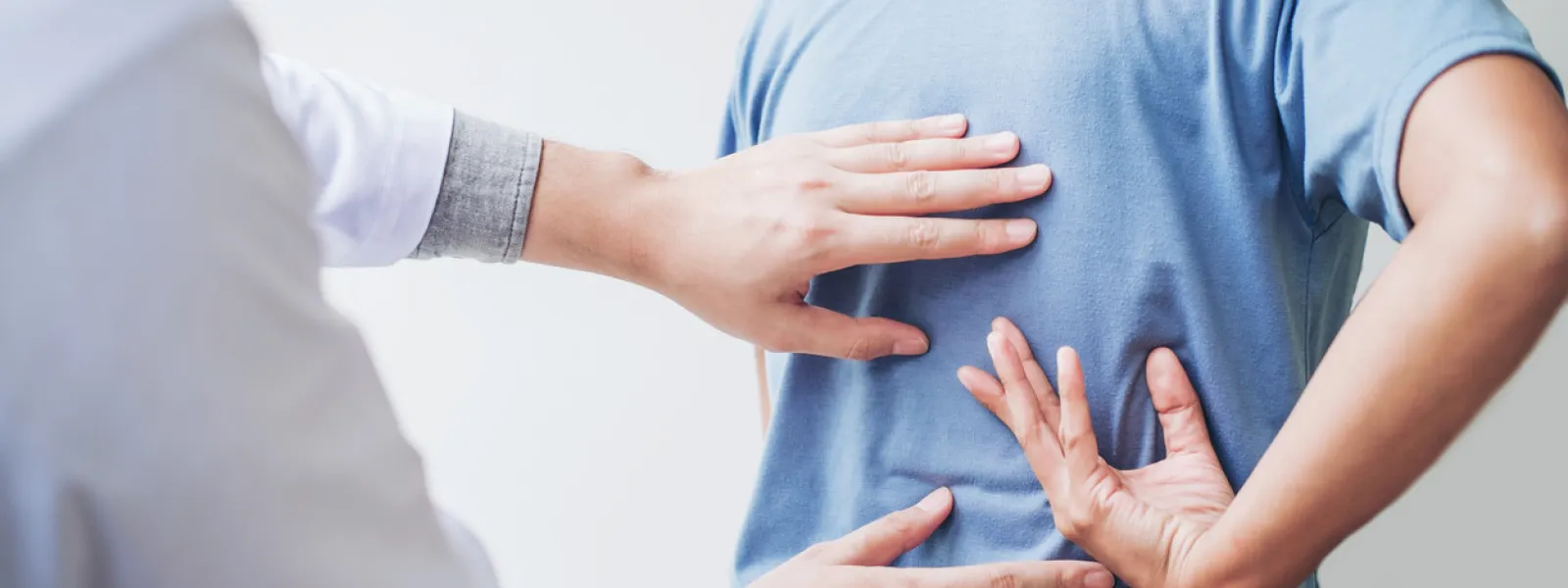 Doctor examining patient's back pain with hands while patient holds lower back in discomfort