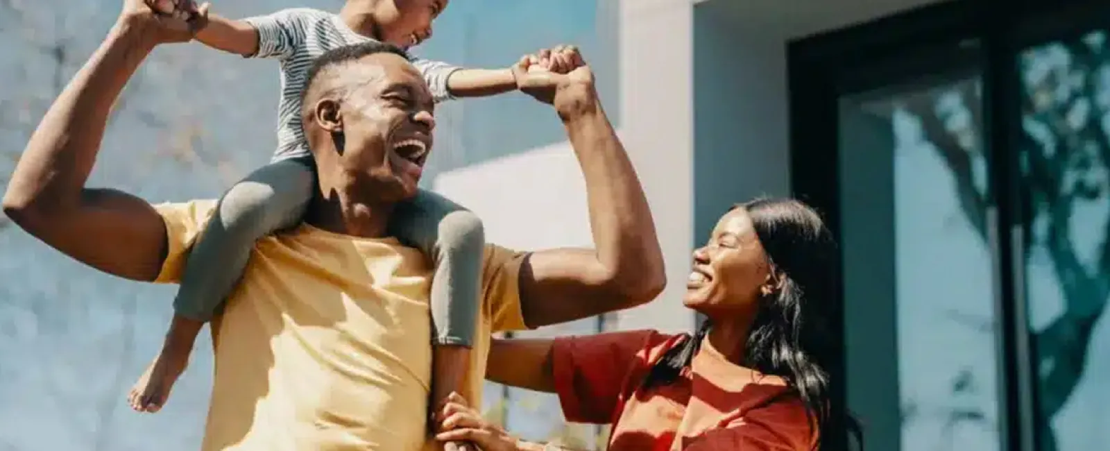 Happy family outdoors with father carrying daughter on shoulders and mother smiling beside them