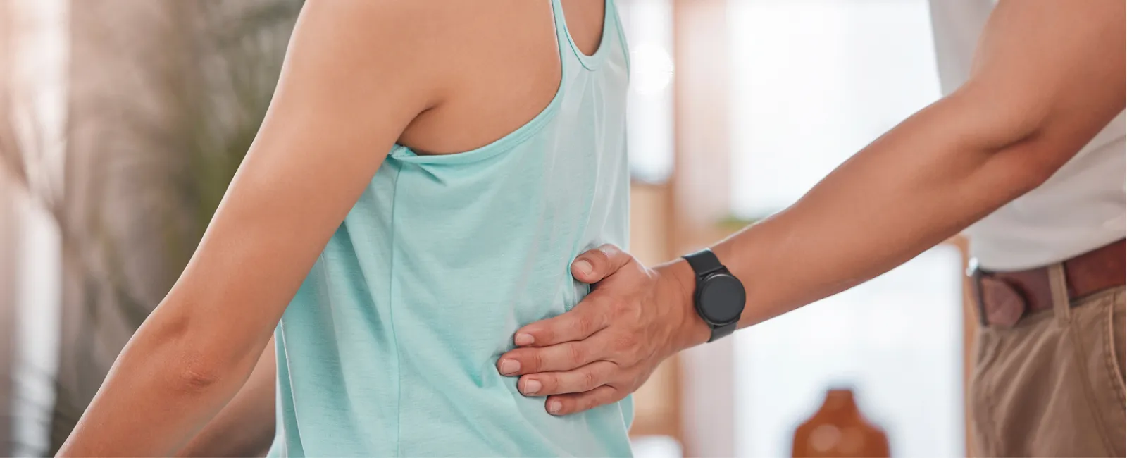 Therapist adjusting woman's posture during physiotherapy session in bright, modern clinic interior with natural light.