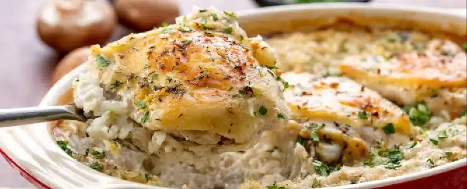 Creamy baked chicken and rice casserole with golden cheese crust garnished with fresh herbs in a red dish