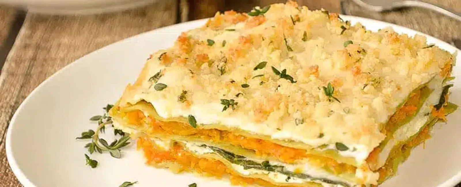 Close-up of a creamy vegetable lasagna slice garnished with herbs on a white plate with a fork.