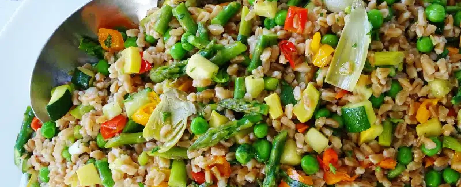 Close-up of a colorful vegetable and grain salad with peas, asparagus, peppers, and zucchini in a bowl.