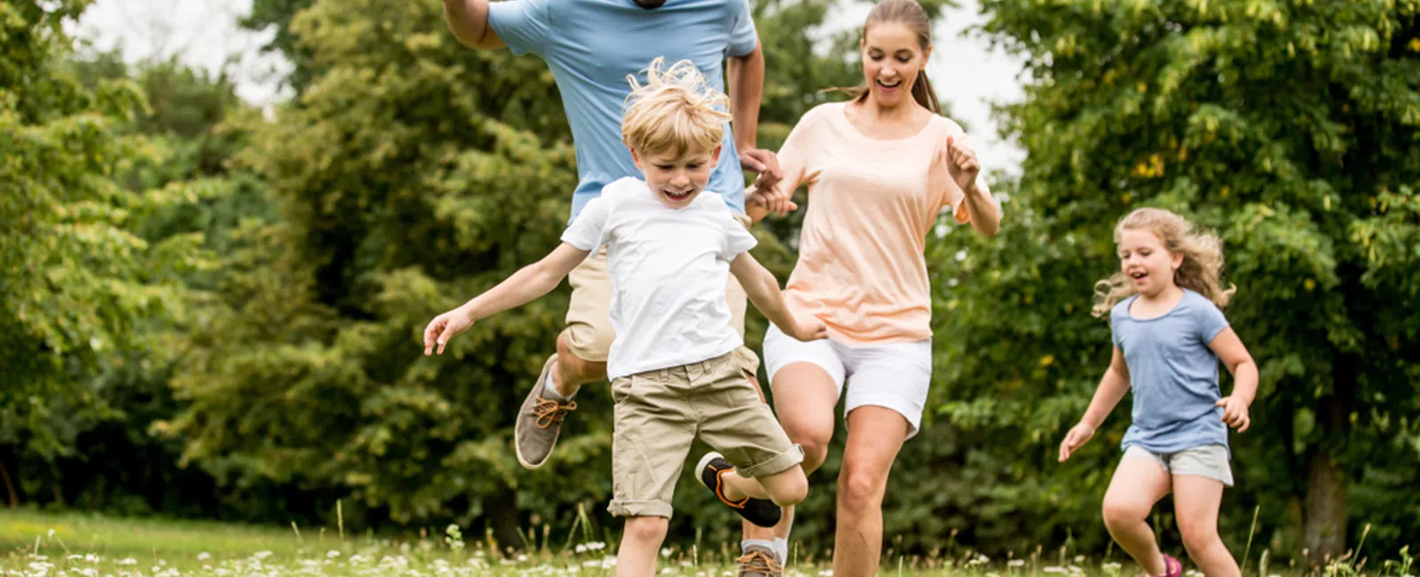 Family of four happily playing soccer together outdoors on a green field with trees in the background