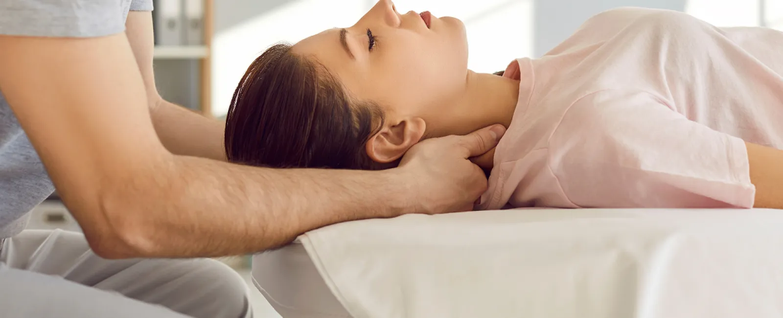 Therapist performing neck massage on a woman lying relaxed on a treatment table.