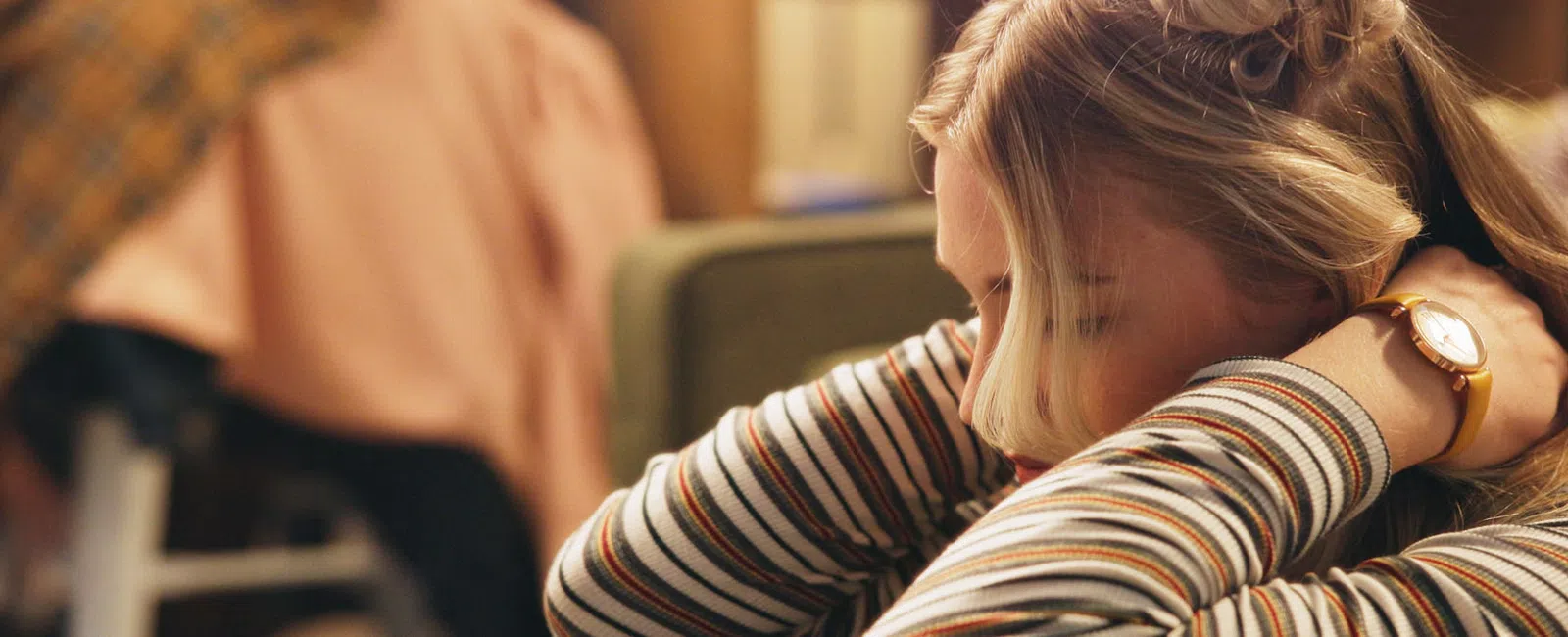 Young woman resting her head on crossed arms wearing a striped shirt in a cozy indoor setting.