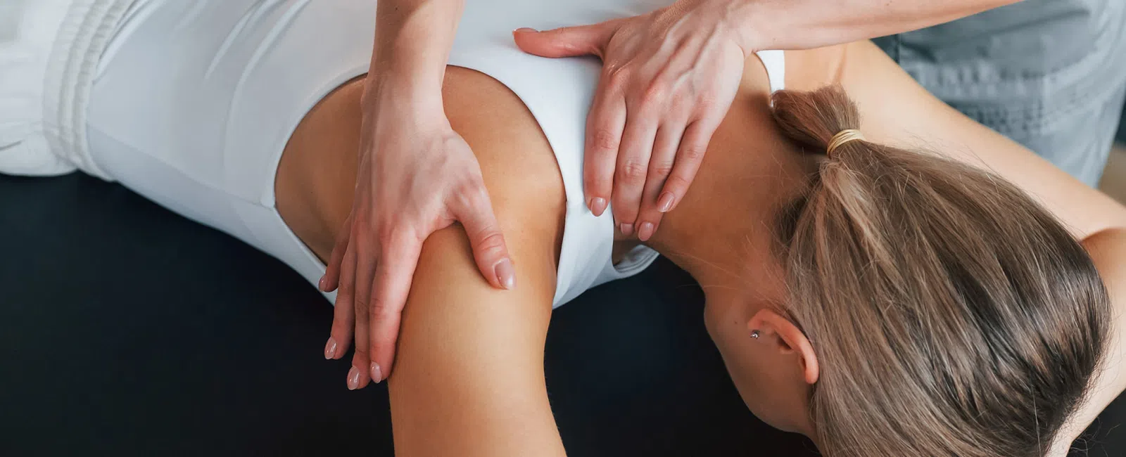 Therapist performing shoulder massage on woman lying face down on a treatment table