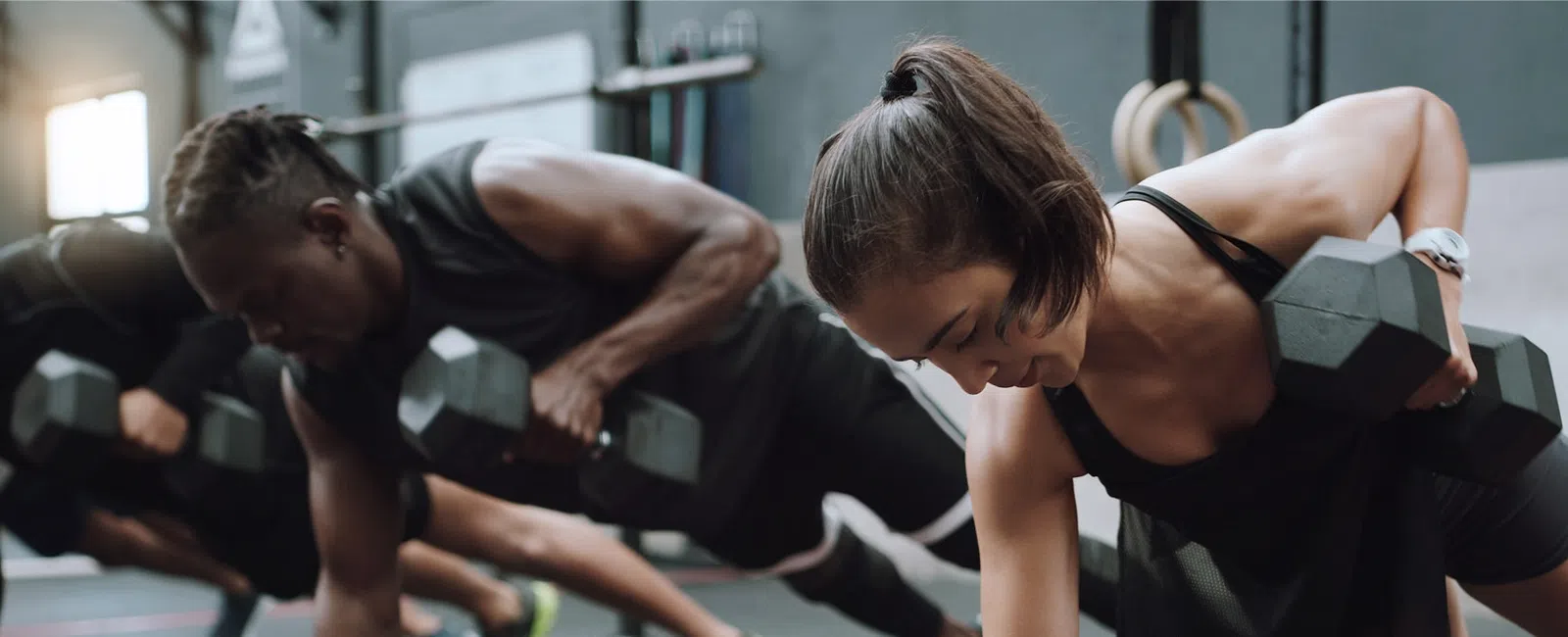 People performing dumbbell renegade rows in a gym with focused expressions and athletic attire.