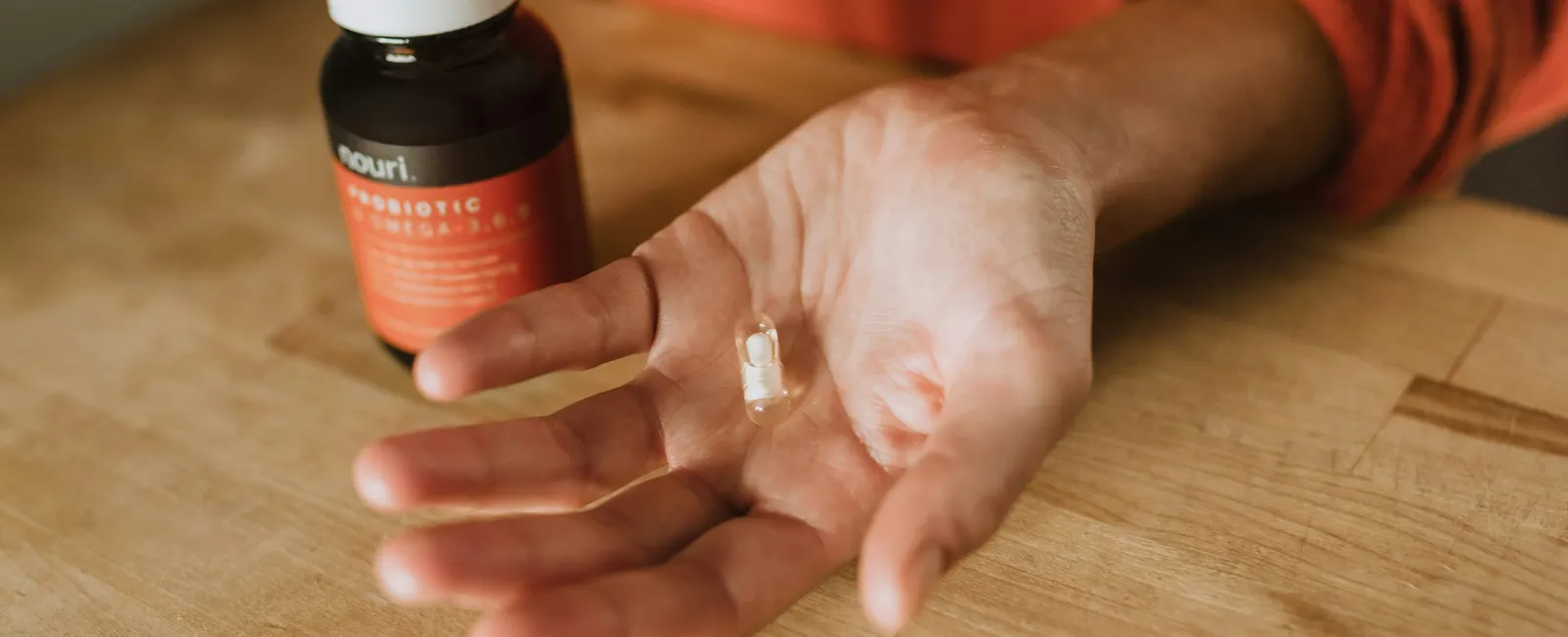 Hand holding a clear probiotic capsule with a bottle labeled probiotic supplement on a wooden table