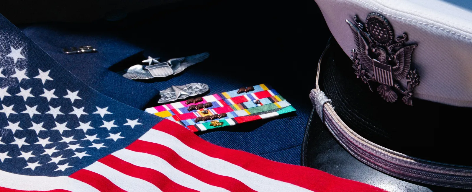 United States Navy officer's uniform with rank insignia, ribbons, American flag, and white service cap.