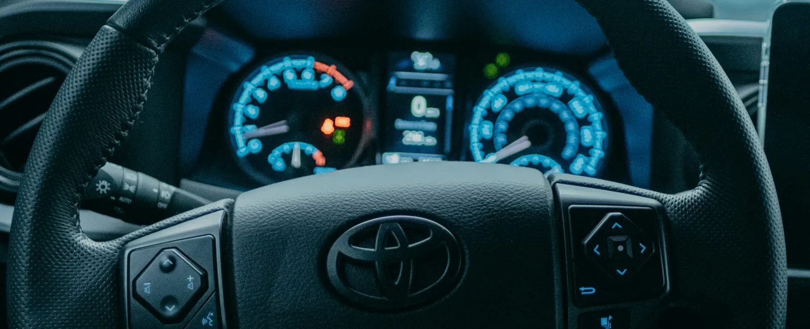 View of a Toyota steering wheel and dashboard with rain drops on the windshield in a parked car.