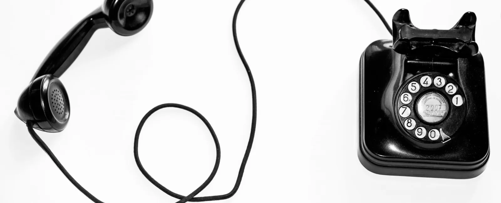 Black vintage rotary dial telephone with detached handset and coiled cord on white background.