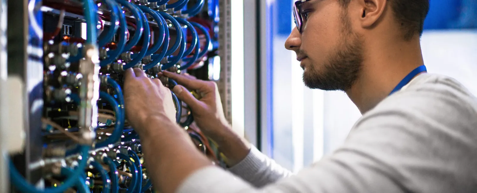 Technician adjusting cables in a server room, maintaining network hardware and connectivity for data systems.