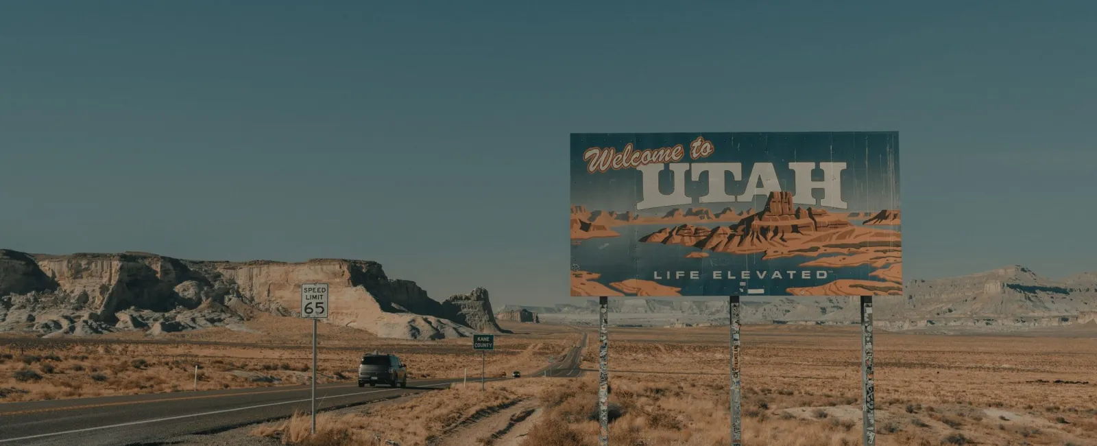 Welcome to Utah roadside sign with desert landscape and clear blue sky in background under bright daylight.