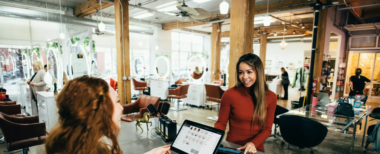 Customer making a payment at a stylish hair salon reception with modern decor and friendly staff member.