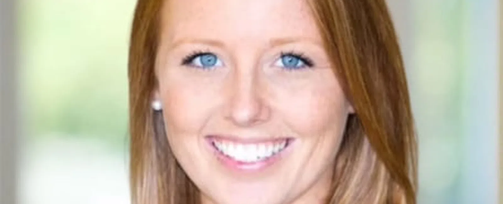 Smiling young woman with long red hair and blue eyes wearing a black top in a softly blurred background