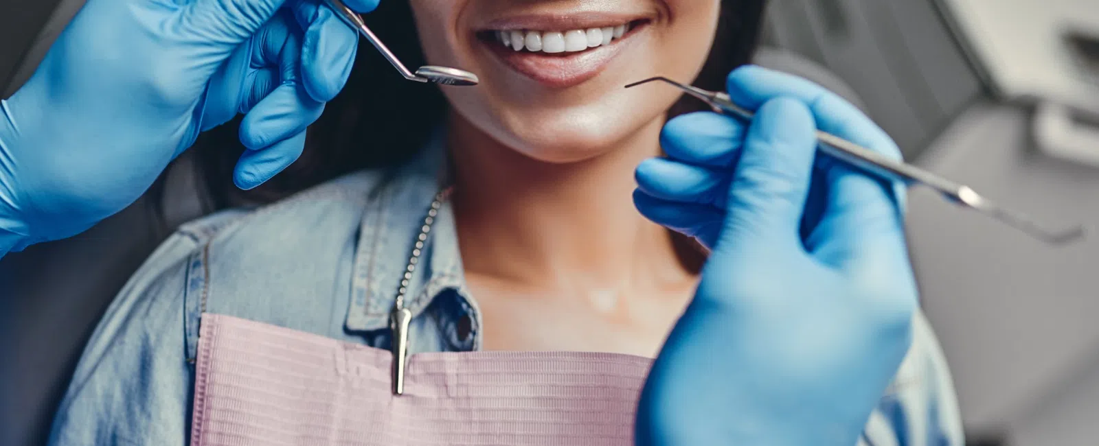 Smiling woman at dental checkup with dentist's gloved hands holding dental tools near her teeth
