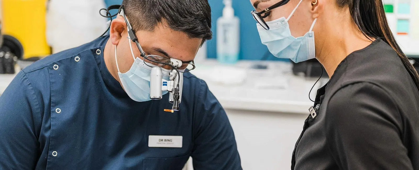 Dentist and assistant in protective gear performing dental procedure on patient in modern clinic.